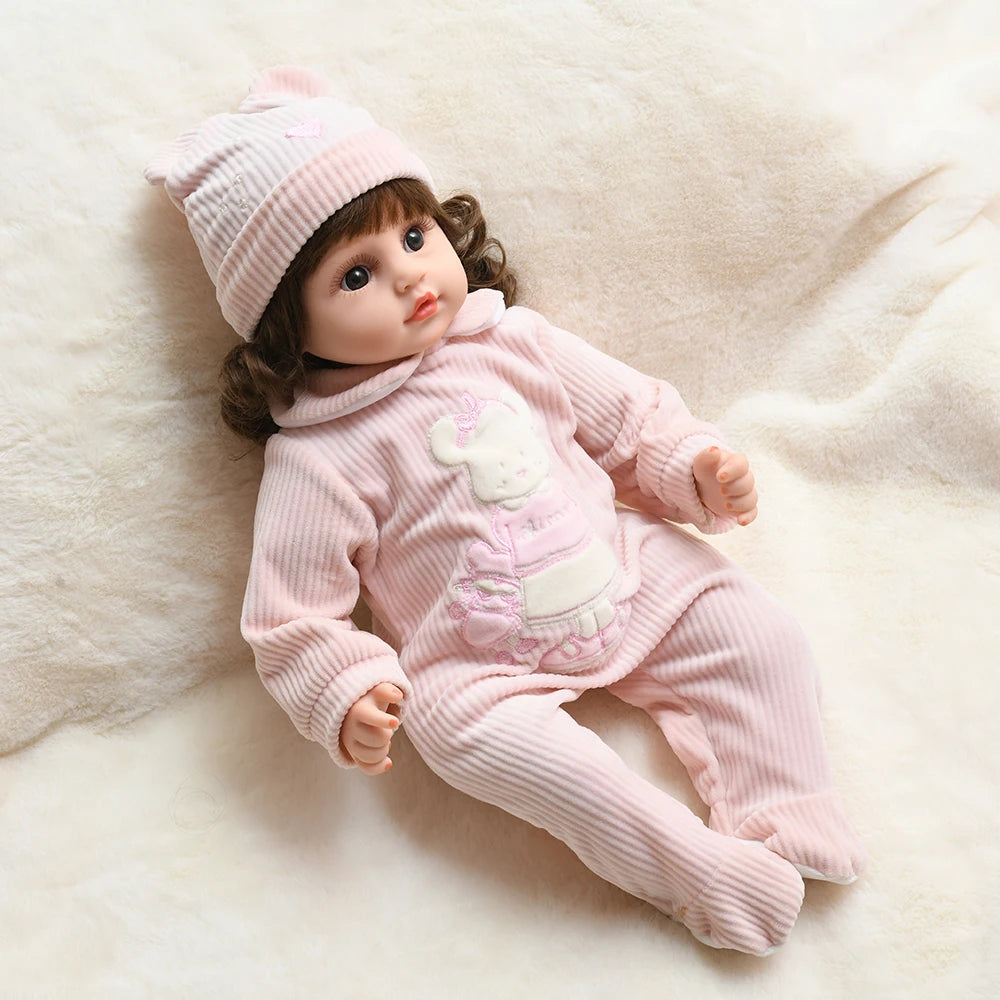 A pink baby doll wearing a matching pink romper and hat, lying on a white fluffy surface.