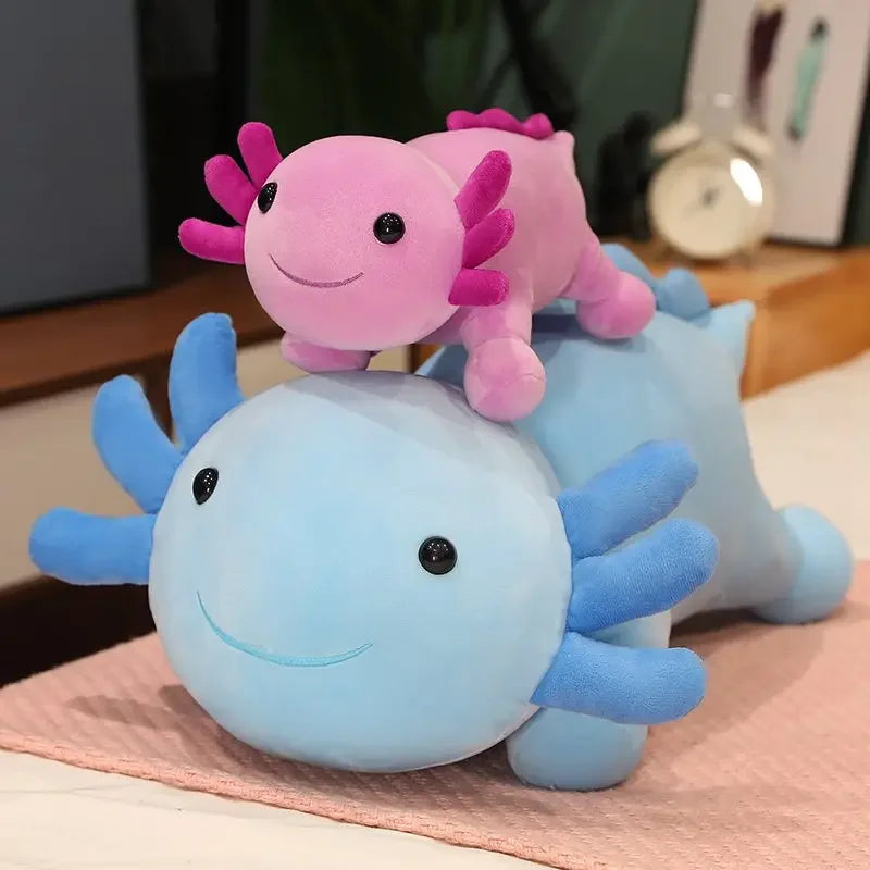 A set of three colorful axolotl plush toys in pink, purple, and blue sitting on a light pink surface.