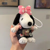 A white dog plush toy with black fur, a pink bow, and a small book charm being held by a hand.