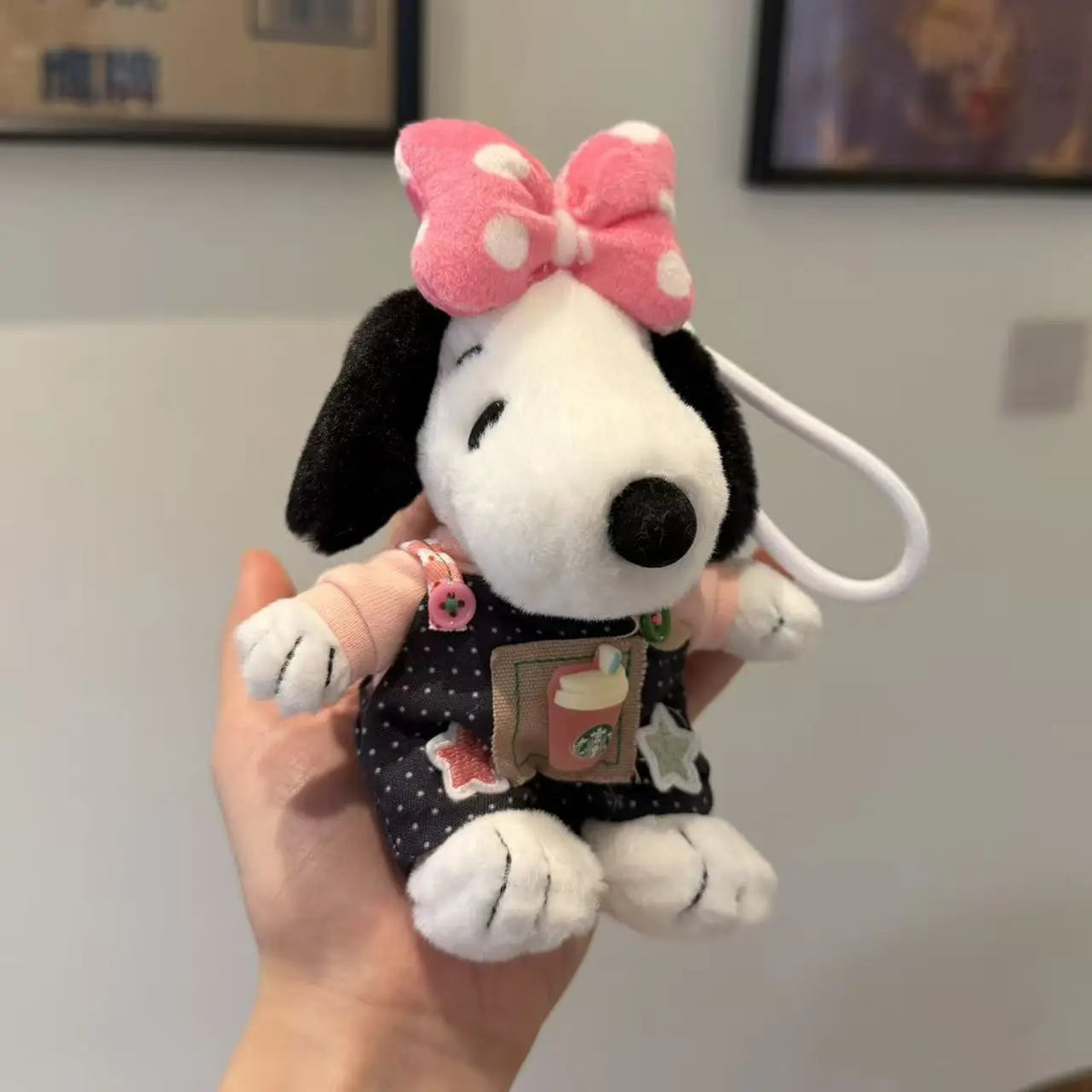 A white dog plush toy with black fur, a pink bow, and a small book charm being held by a hand.