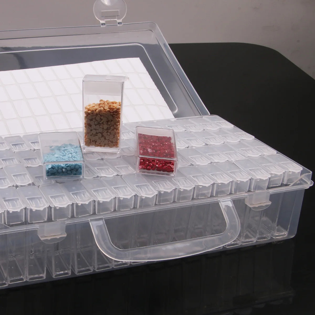 A clear storage box for diamond painting supplies featuring multiple organizer trays holding colored beads and stones.
