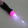 A close-up of a black and pink LED crochet hook tool with a glowing purple tip.