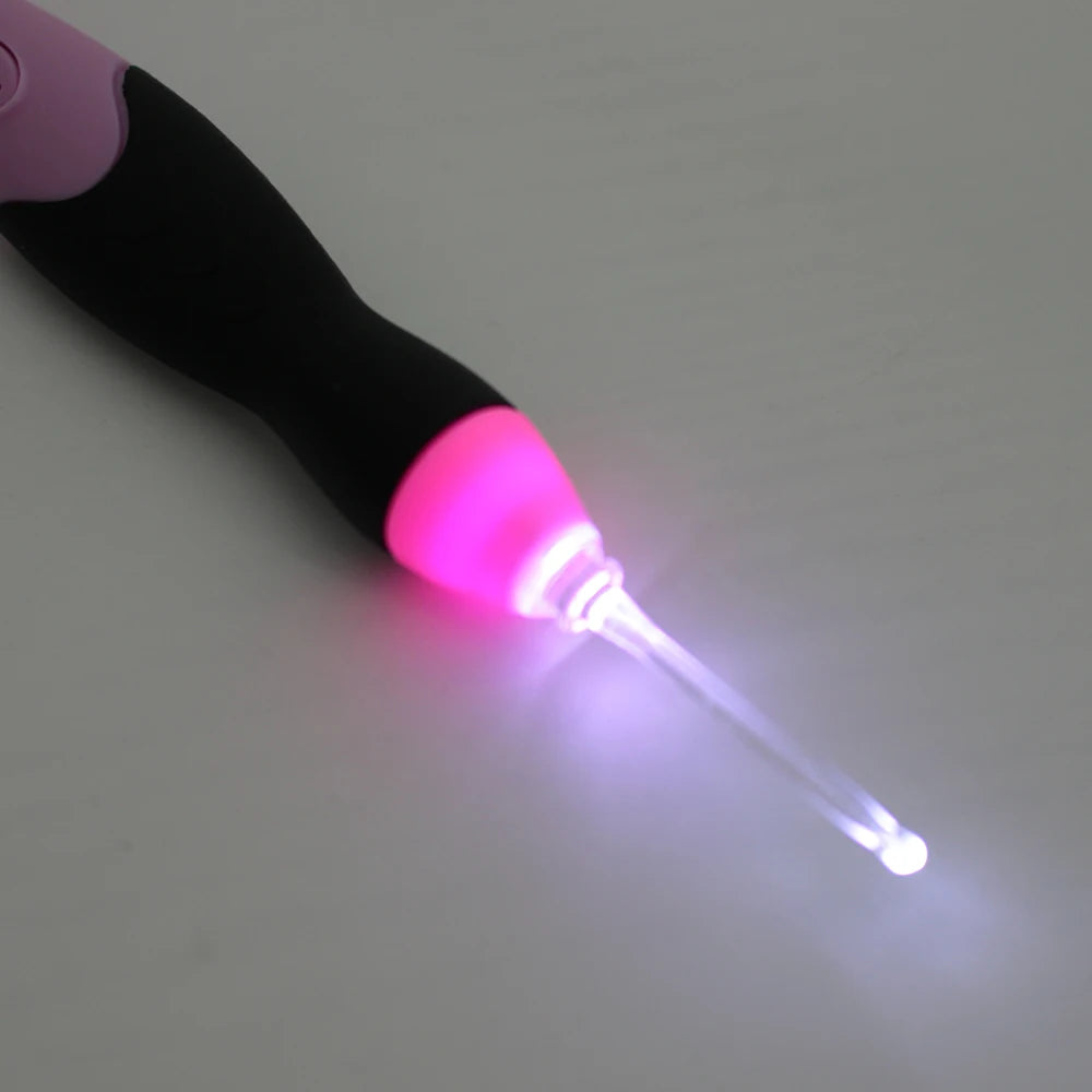 A close-up of a black and pink LED crochet hook tool with a glowing purple tip.