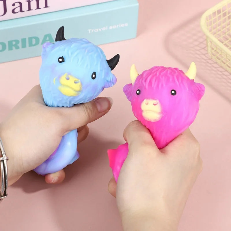 A hand holds a purple glitter cow squishy toy, next to a pink glitter cow squishy toy and a box.