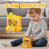 A young boy is playing a yellow mini claw machine toy with colorful plastic items on a carpet.