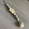 A string of wooden and silicone beads forms a clip for a baby pacifier.