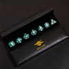 A black box containing a set of polyhedral dice with green and silver accents.