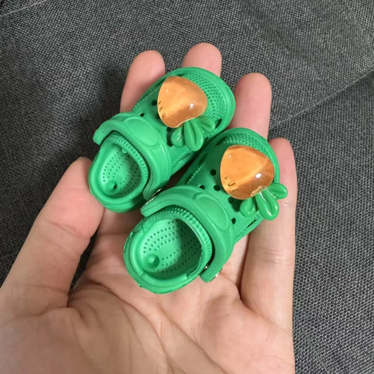 A pair of bright green fashion slippers for 1/6 BJD dolls with gold accents being held in a hand.