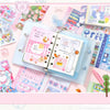 A collection of pink and blue kawaii cartoon stickers, writable notes, and a clear plastic notebook for DIY scrapbooking.