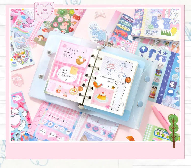 A collection of pink and blue kawaii cartoon stickers, writable notes, and a clear plastic notebook for DIY scrapbooking.