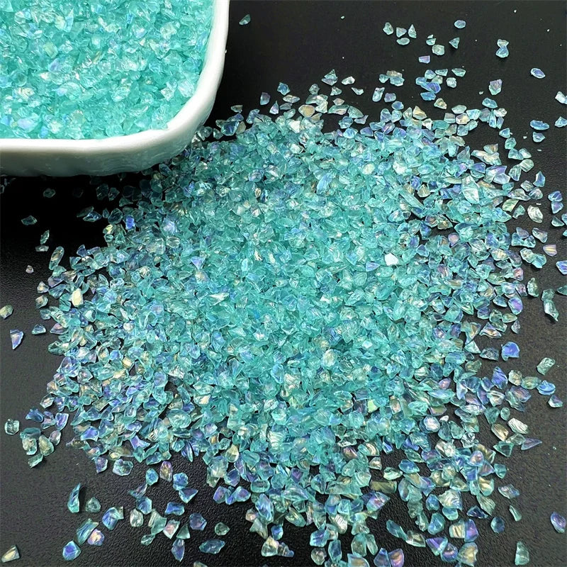 Crushed turquoise blue glass crystals scattered on a dark surface next to a white bowl