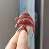 A hand holds a red rhinestone turtle brooch pin with a gold-colored curved shape.
