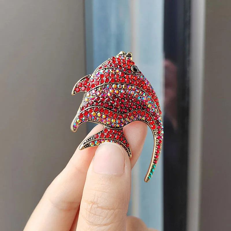 A hand holds a red rhinestone turtle brooch pin with a gold-colored curved shape.