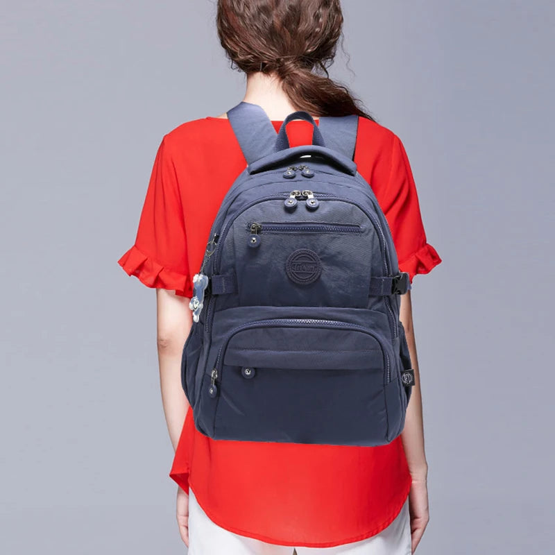Une femme porte un sac à dos de voyage bleu marine et durable avec des accents gris sur une chemise rouge.