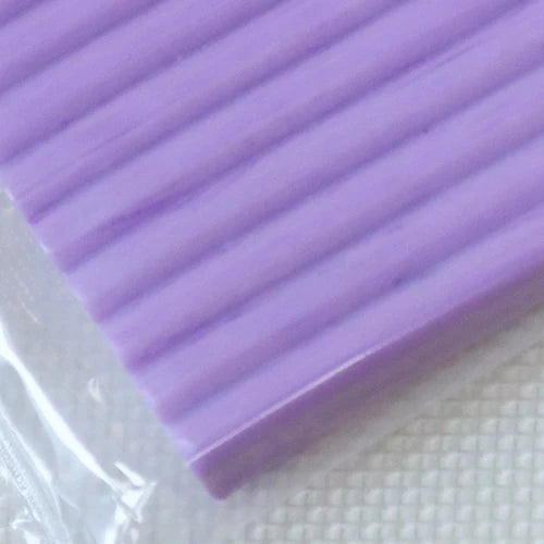 A close-up of a purple, ridged polymer clay block resting on a white surface.