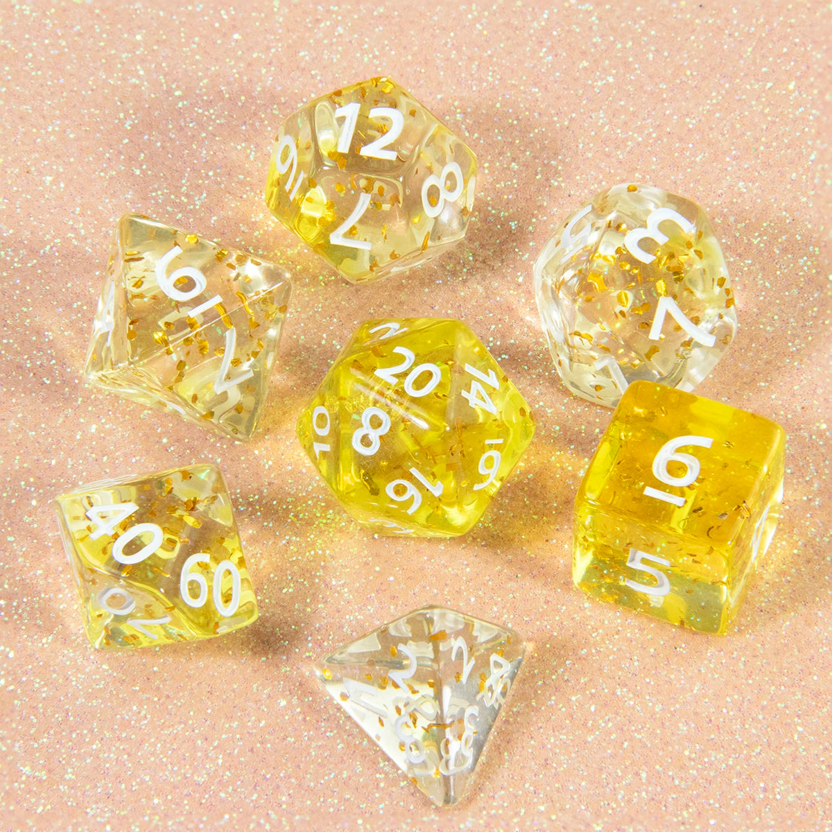 A collection of clear yellow glitter polyhedral dice including D4, D6, D8, D10, D12, and D20 scattered on a pink surface.