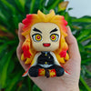 A hand holds an action figure of the Demon Slayer character Tanjirou with spiky yellow and red hair and glowing eyes.