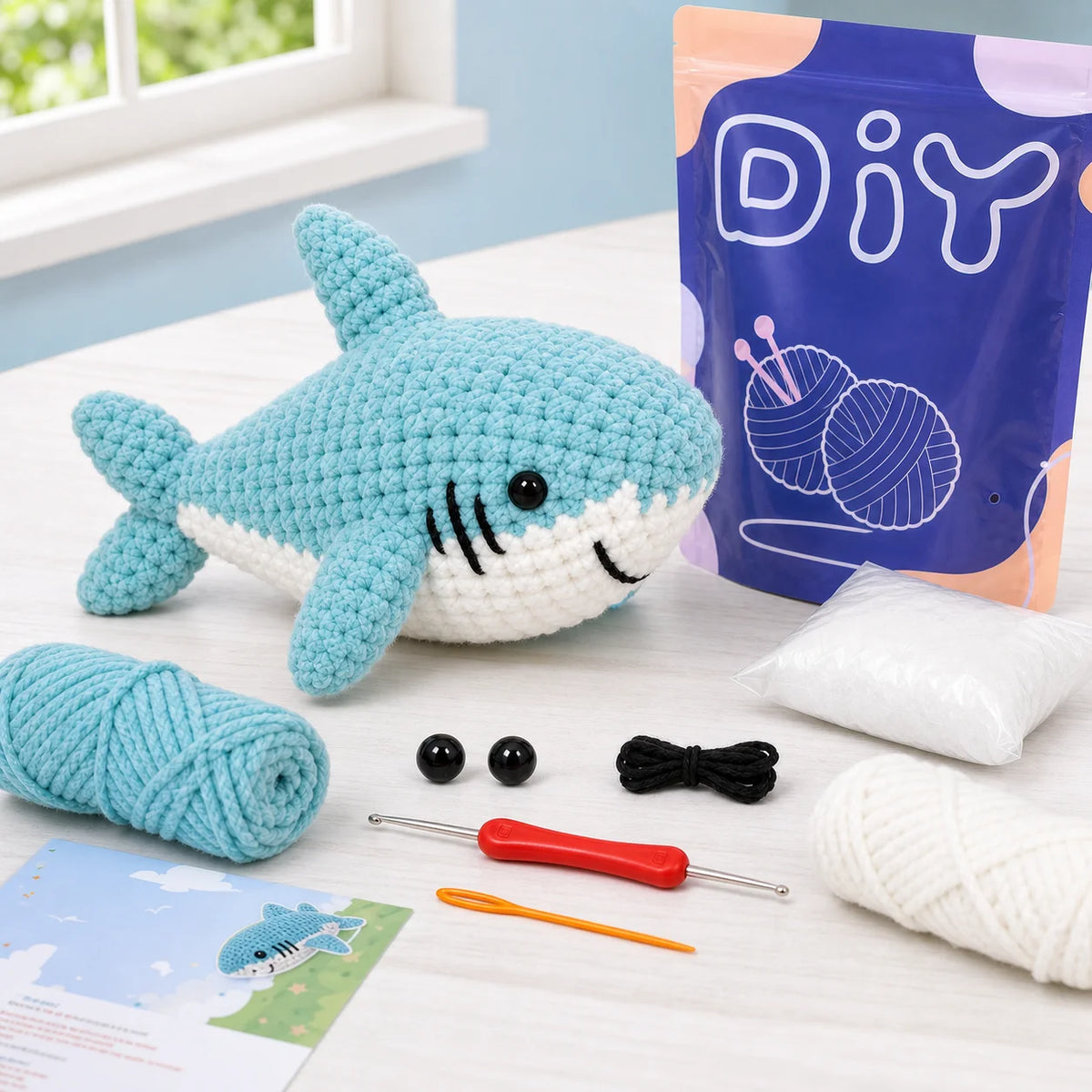 Kit de crochet débutant pour animaux amigurumi, montrant le fil, les aiguilles et un poisson-requin bleu terminé.
