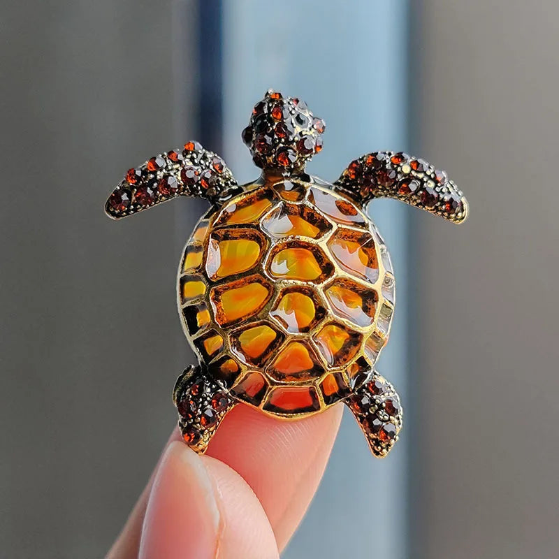 A detailed rhinestone turtle brooch pin with an amber shell and textured head is held by a hand.