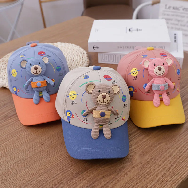 Three colorful toddler bear baseball caps in blue, pink, and yellow resting on a wooden table.