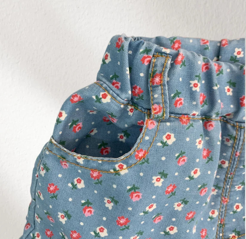 A close-up of a girl's blue floral print sleeveless shirt and shorts set with gathered fabric details.