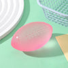 A pink football-shaped squishy fidget toy resting on a light green surface next to a white plate and a wire basket.