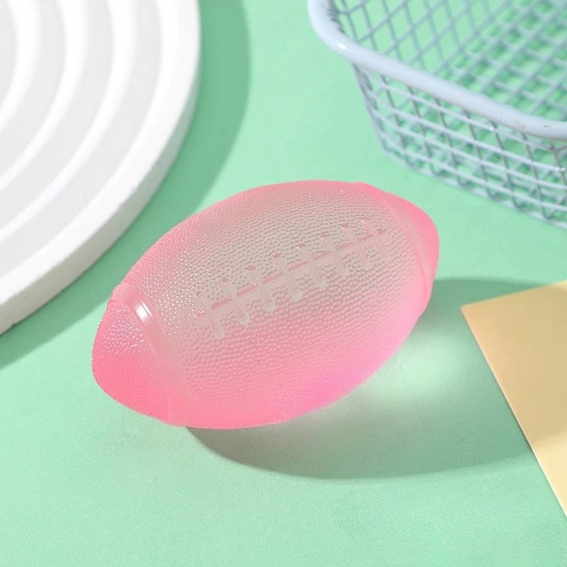 A pink football-shaped squishy fidget toy resting on a light green surface next to a white plate and a wire basket.