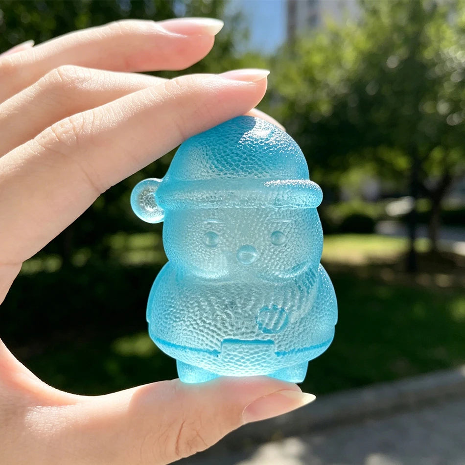 A hand holds a translucent blue squishy toy shaped like a cute, round creature outdoors.