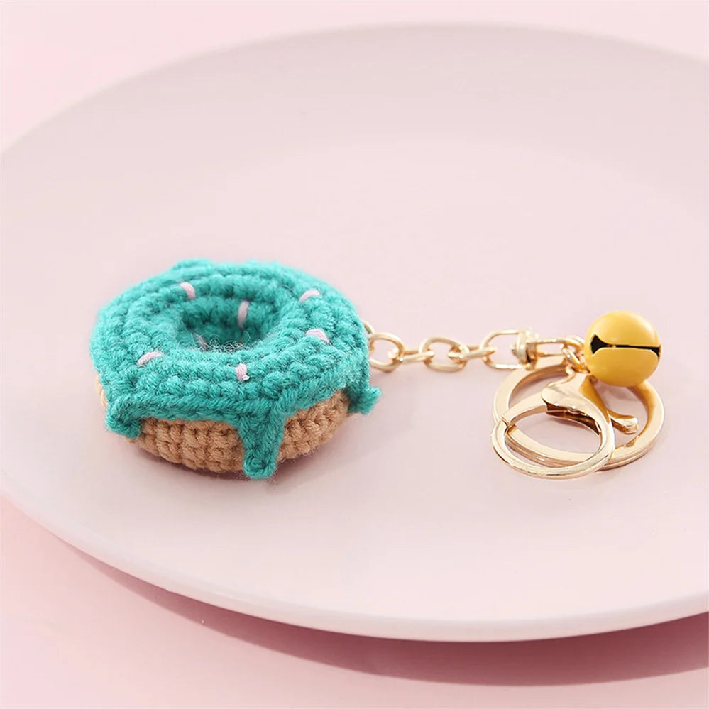 A teal crochet fruit pendant with pink accents attached to a gold-colored chain.