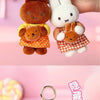 A white Miffy plush keychain charm with brown ears and a yellow outfit is being held by a hand.