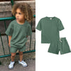 A child wearing a sage green short sleeve top and matching shorts outdoors.