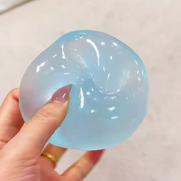 A hand is squeezing a translucent light blue stress relief squishy sensory ball.