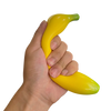 A hand is holding a bright yellow squishy banana stress relief toy.
