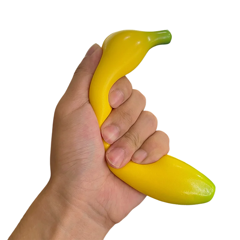 A hand is holding a bright yellow squishy banana stress relief toy.