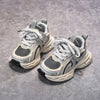 A pair of light gray and white breathable mesh kids running sneakers with cushioned soles resting on a gray surface.