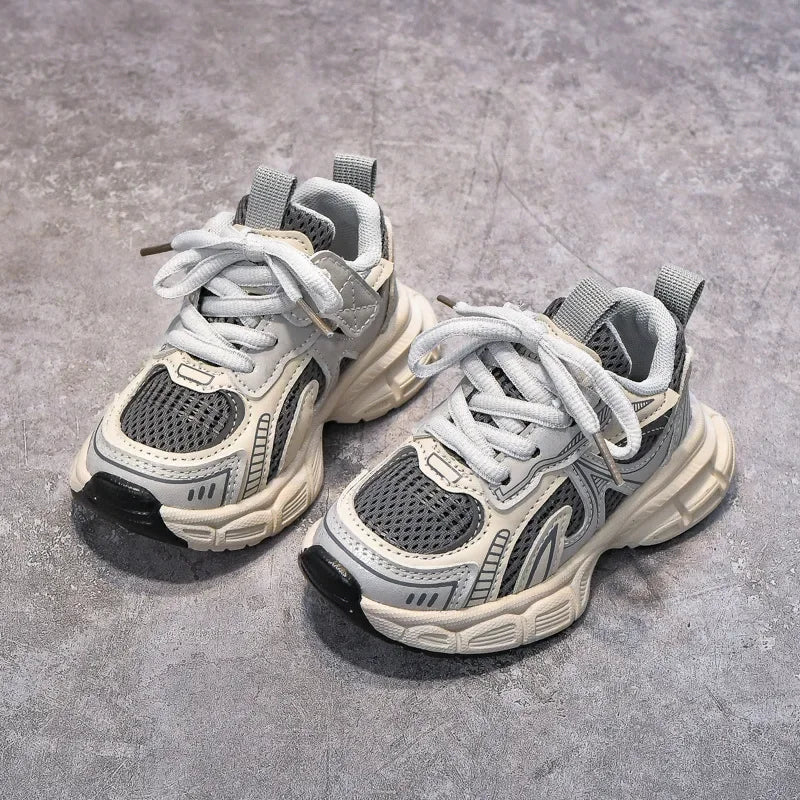 A pair of light gray and white breathable mesh kids running sneakers with cushioned soles resting on a gray surface.