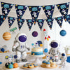 A collection of outer space astronaut party décor including flags, balloons, and figures on a white table.