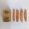 Three miniature baguette loaves are displayed next to a brown bakery tag.