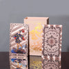 A collection of gold foil tarot cards in rose pink finish displayed next to a cardboard box.
