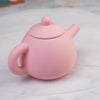 A pink silicone pretend play tea set teapot with a lid and spout resting on a white surface.