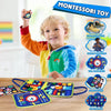 A smiling toddler holds up a Montessori felt activity busy book with a dinosaur theme on a wooden table.