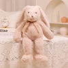 A soft, light pink bunny plush toy with long ears sitting on a white lace tablecloth.