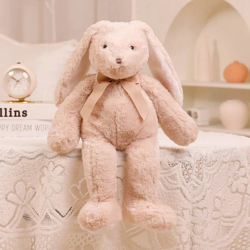 A soft, light pink bunny plush toy with long ears sitting on a white lace tablecloth.