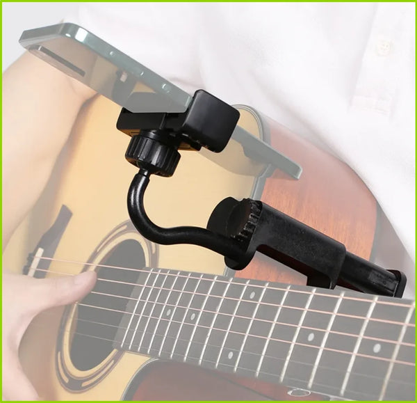 A hand is adjusting an adjustable guitar and instrument phone mount attached to the neck of an acoustic guitar.