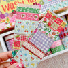A hand holds a collection of colorful strawberry patterned washi tape rolls in a white box.