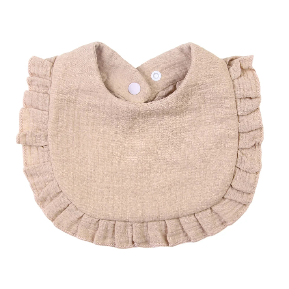 A light beige ruffled muslin cotton baby bib with an adjustable snap closure.