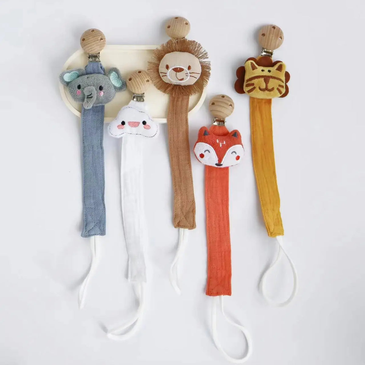 A set of elephant, lion, and fox pacifier holders with clips and various colored fabric strings.