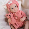 A realistic silicone reborn baby doll wearing a pink knitted fox hat and matching outfit.