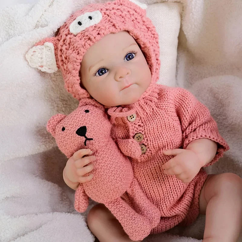 A realistic silicone reborn baby doll wearing a pink knitted fox hat and matching outfit.