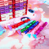 A collection of diamond art pens with various colored and shaped tips arranged in a red storage rack on a pink background.